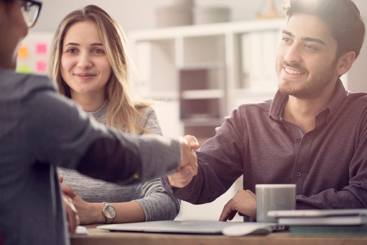 A man and woman shaking hands over a table.