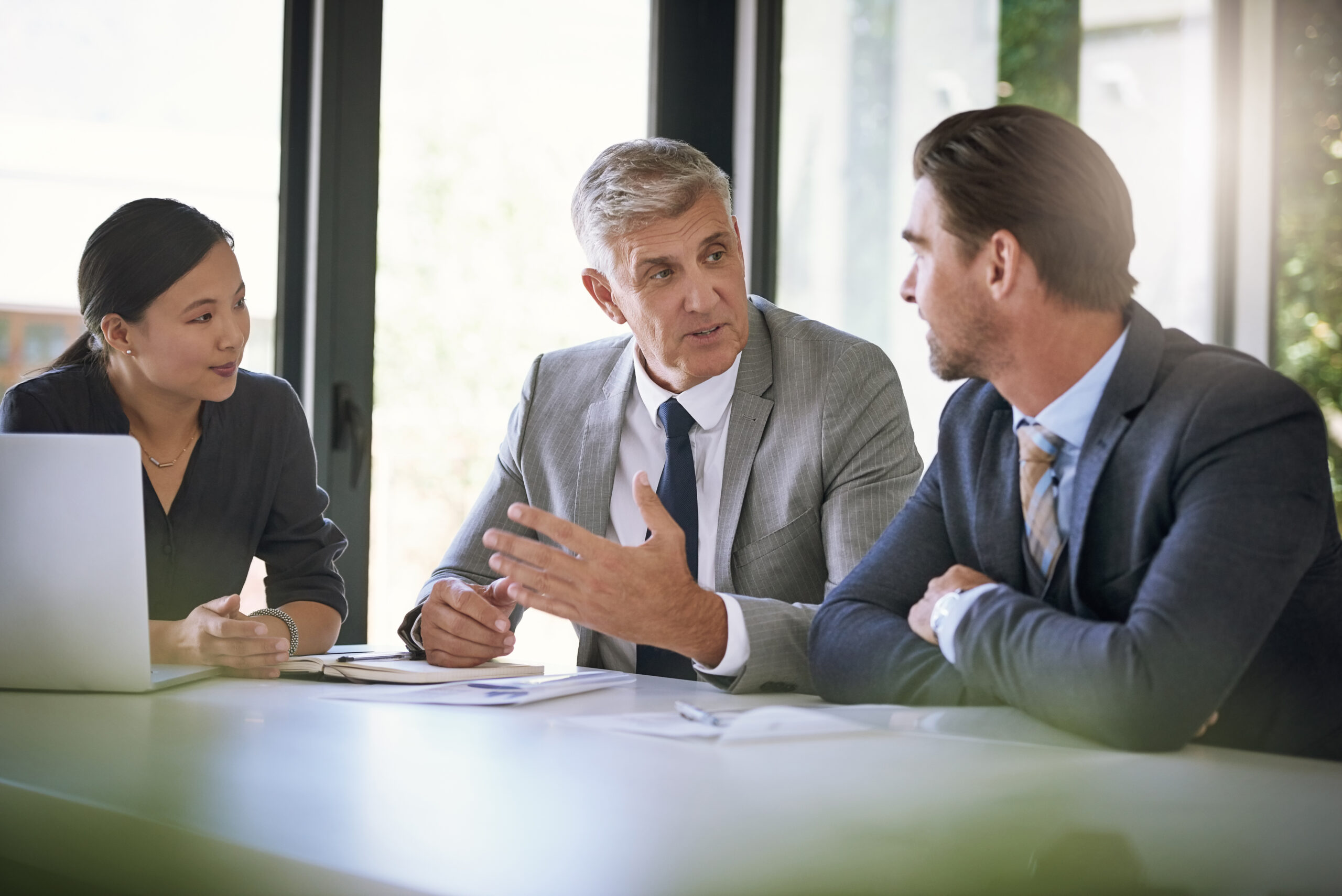 Three men in suits sitting at a table talking to each other.