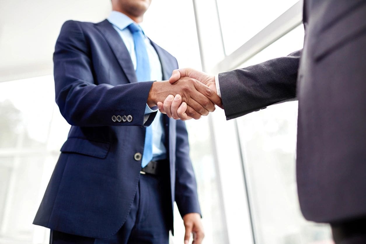 fm=f_wNVRqx6 Two men in suits shaking hands over a window.