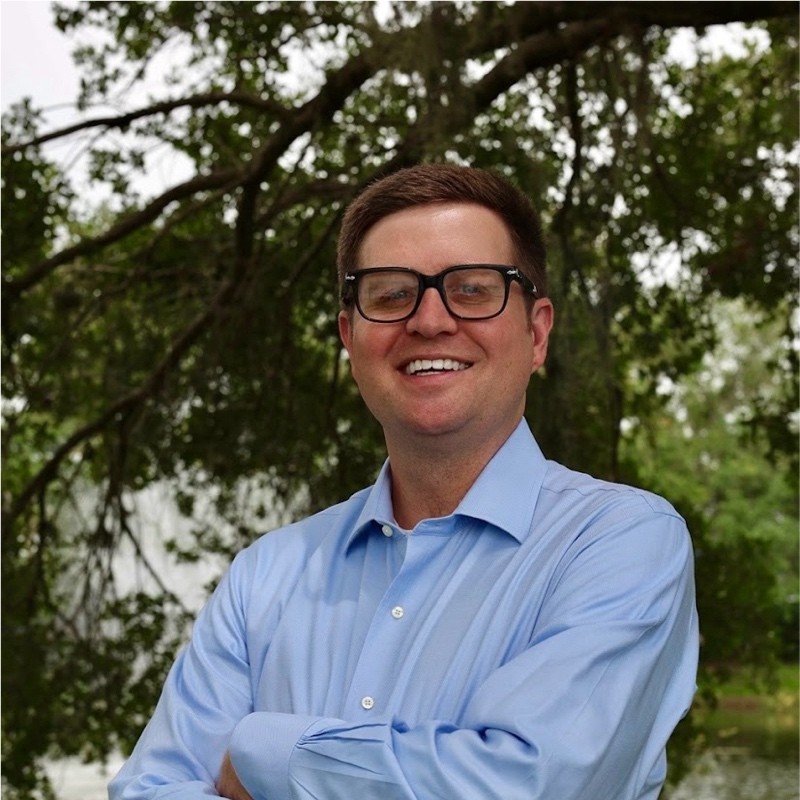 A man in glasses and blue shirt smiling for the camera.