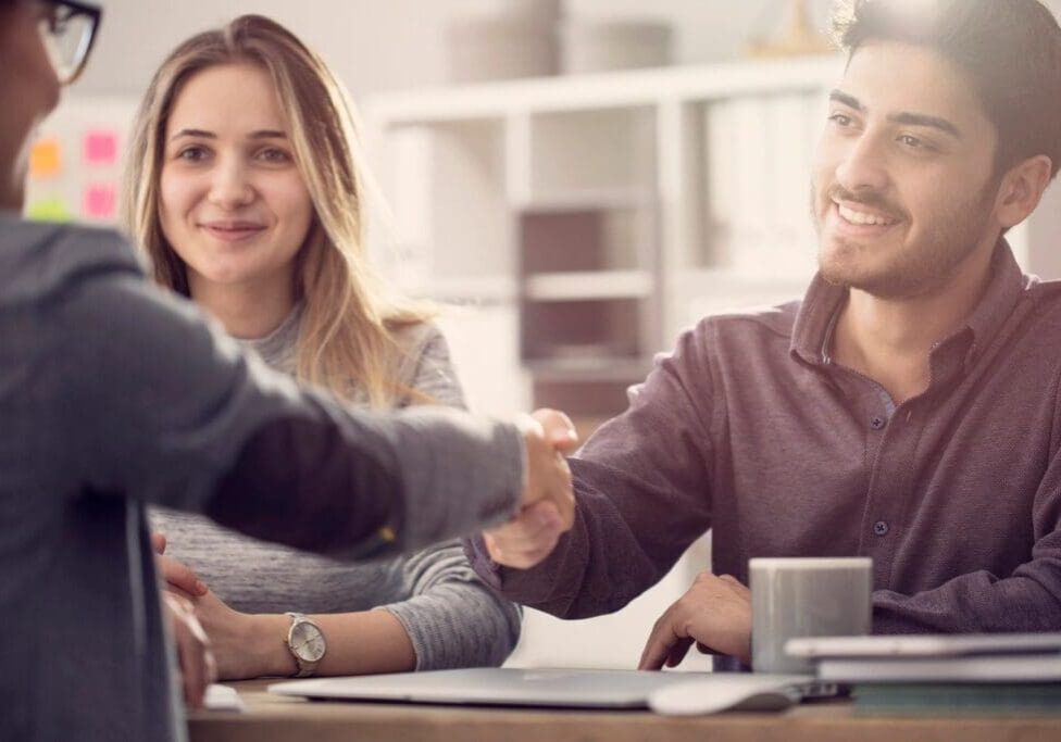 A man and woman shaking hands over a table.